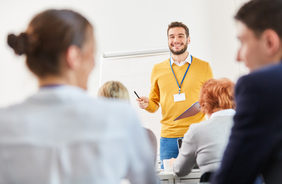 Man in mustard jumper taking questions from people in workshop